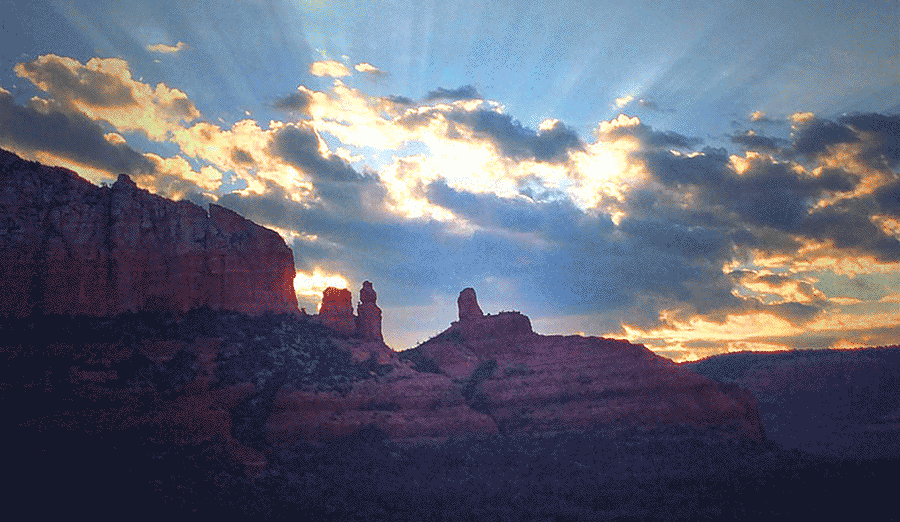 Sedona red rock formations with dramatic sunbeams breaking through clouds at sunset