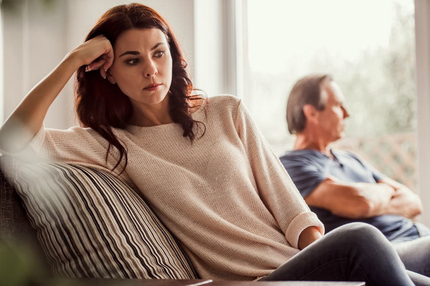a woman looking distressed while a man sits turned away in the background